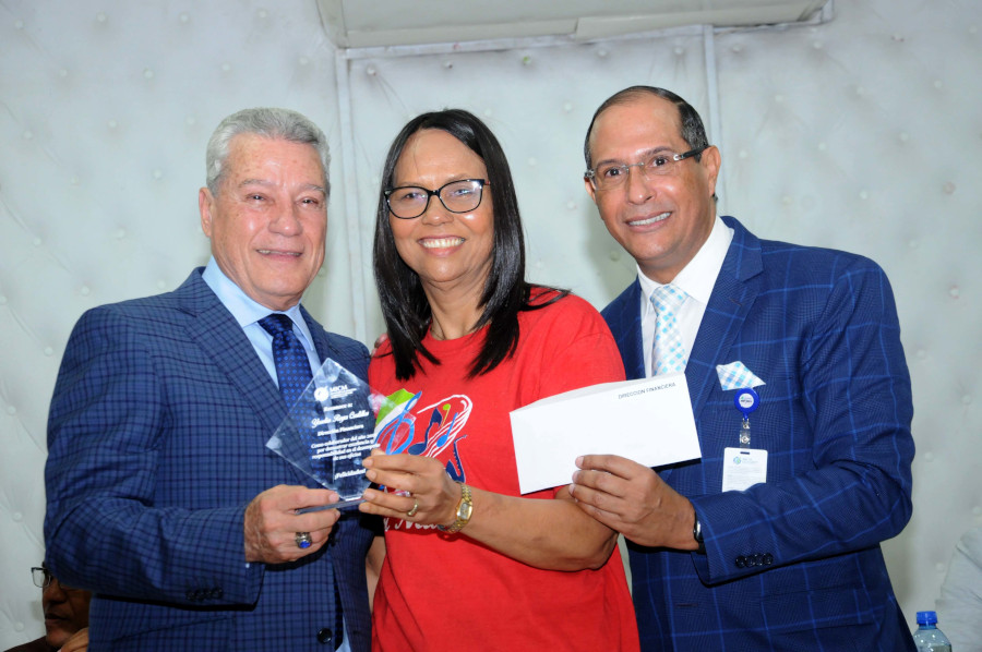 El titular del MICM, Nelson Toca Simó, entrega reconocimiento a la empleada Yoselin Reyes, junto al director Financiero, Manolo Caba.