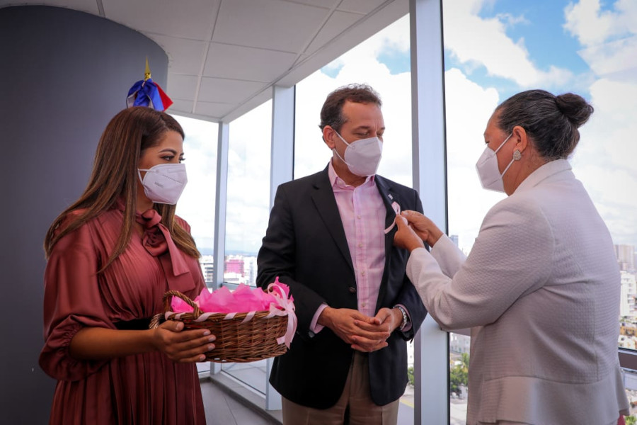 Miguelina Estévez, colaboradora del MICM sobreviviente de cáncer de mamas, le colocó al ministro el lazo rosa, símbolo del tema, junto a Dessirett Fernández.